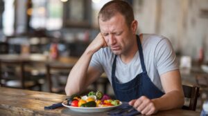 Man sitting at table in disgust looking at a plate of vegetables