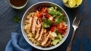 Grilled chicken paired with quinoa and fresh veggies in a large white dinner bowl.