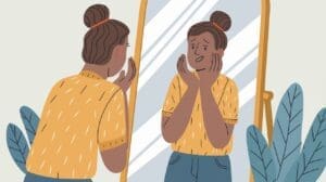 Illustration of a person with a bun hairstyle, wearing a yellow shirt, looking worried at their reflection in a mirror. Emphasizing daily mental health tips, the person holds their face with both hands. Green leafy plants beside the mirror add a touch of calmness.
