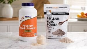 Two containers of psyllium husk powder, ideal for psyllium husk weight loss support, sit on a marble counter. One is a large NOW bottle and the other an It's Just! pouch, each with scoops of powder in front and fruits blurred in the background.